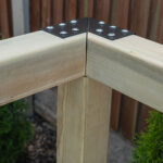 Black three way corner pergola bracket connecting an upright timber post and two horizontal beams